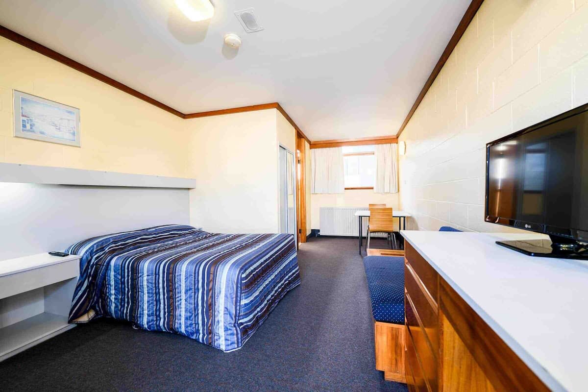 Una habitación de hotel pequeña con una cama individual, un escritorio, un televisor y una kitchenette.