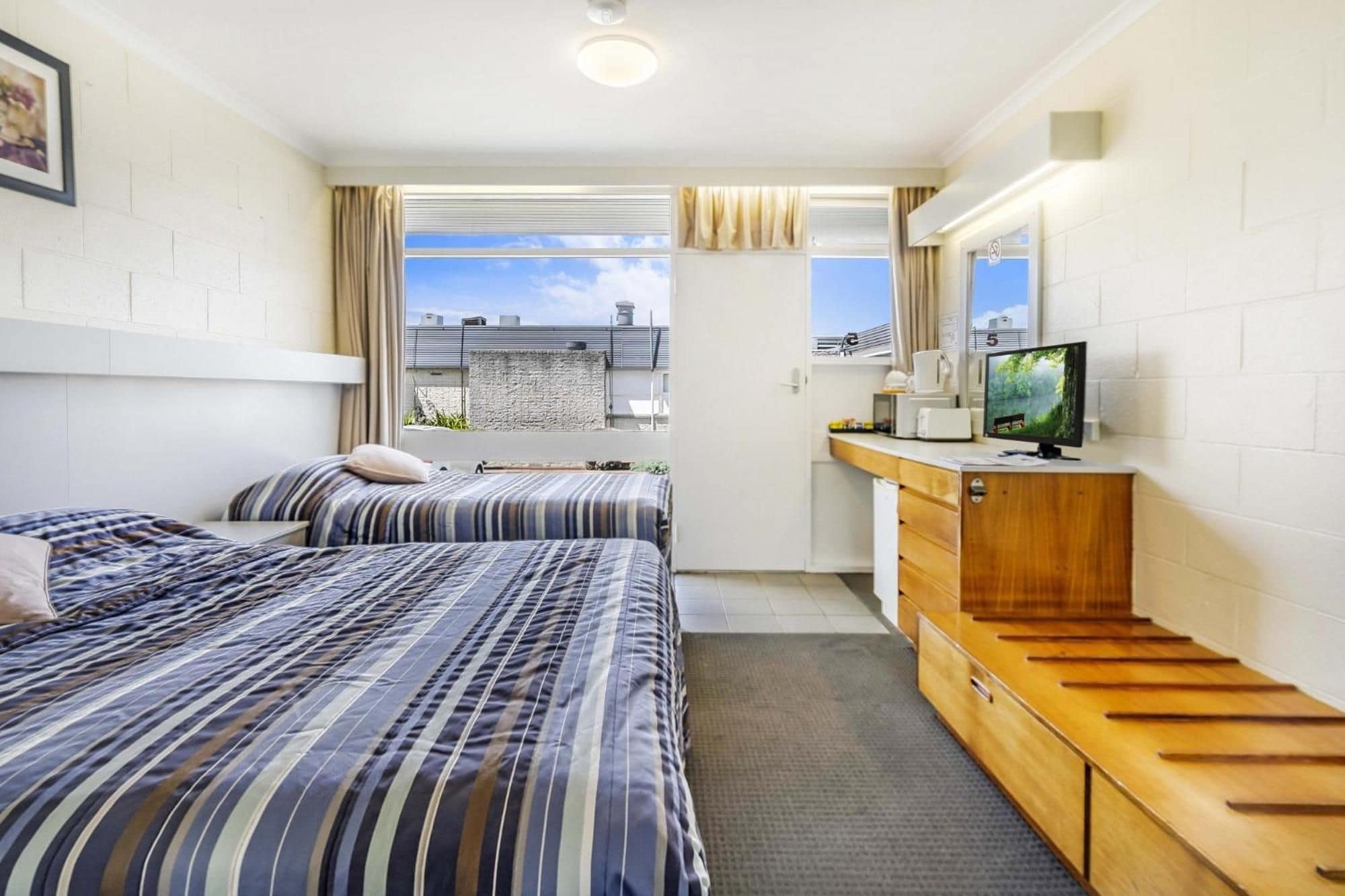 Une chambre d’hôtel avec deux lits, une petite kitchenette, une télévision et une vue sur le paysage urbain.