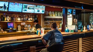 A bar with multiple screens displaying sports and news, a bartender, and a variety of bottles and glasses on the shelves. - Top of the Town Hotel Motel (Upper Burnie)