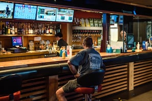 A bar with multiple screens displaying sports and news, a bartender, and a variety of bottles and glasses on the shelves. - Top of the Town Hotel Motel (Upper Burnie)