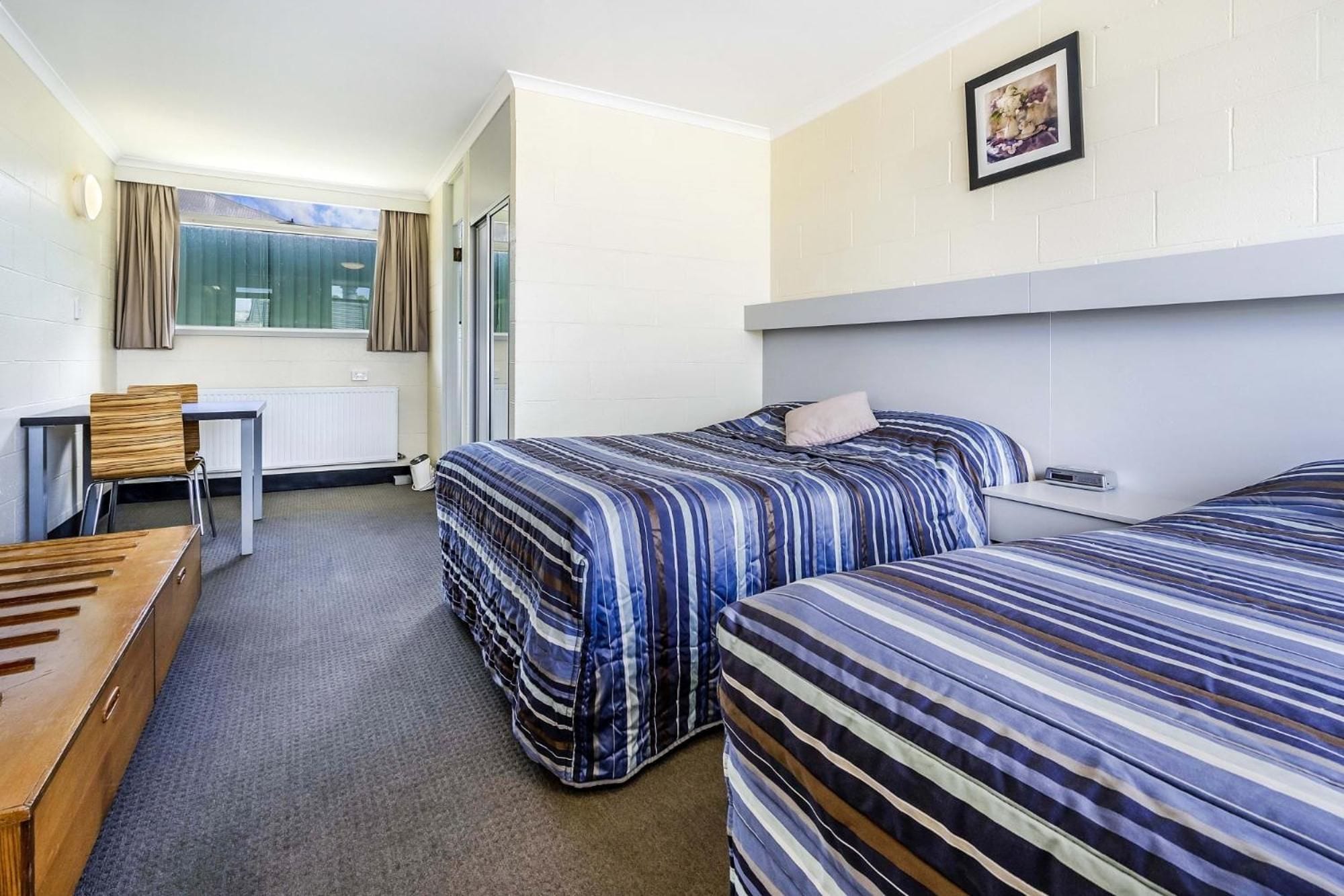 Une chambre d’hôtel avec deux lits, un bureau, une chaise et une fenêtre avec des rideaux.