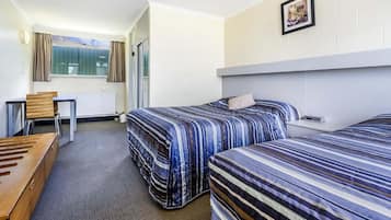 Une chambre d’hôtel avec deux lits, un bureau, une chaise et une fenêtre avec des rideaux.