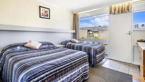 Habitación de hotel con dos camas, una ventana con cortinas, un escritorio pequeño y un cuadro en la pared.