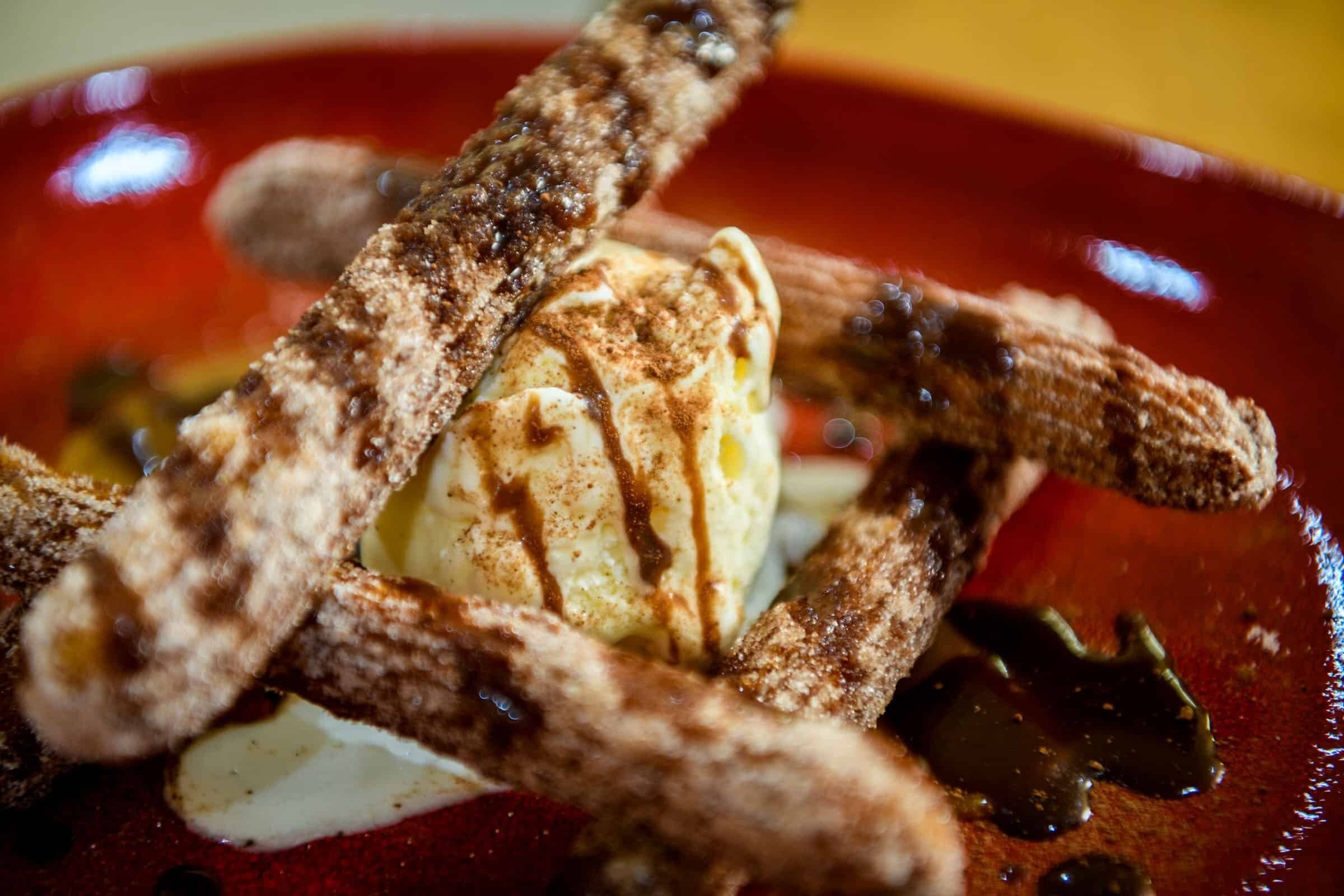 Un postre con churros, helado y salsa de chocolate en un plato.