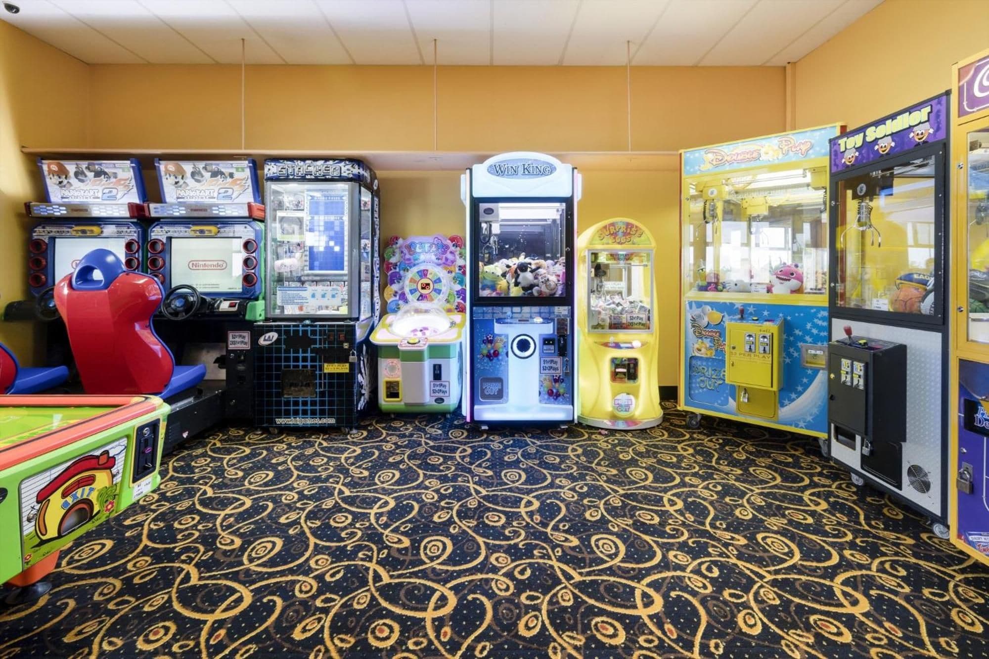 A row of arcade machines in a room with patterned carpet flooring.