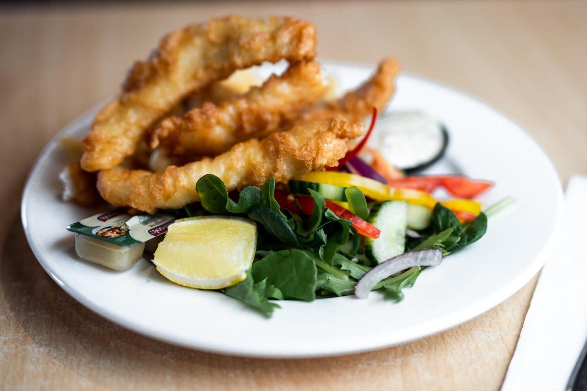 Un plato con pescado frito, ensalada y una rodaja de limón.
