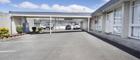 Un estacionamiento con zona techada, un edificio de fachada de piedra y cielo despejado.