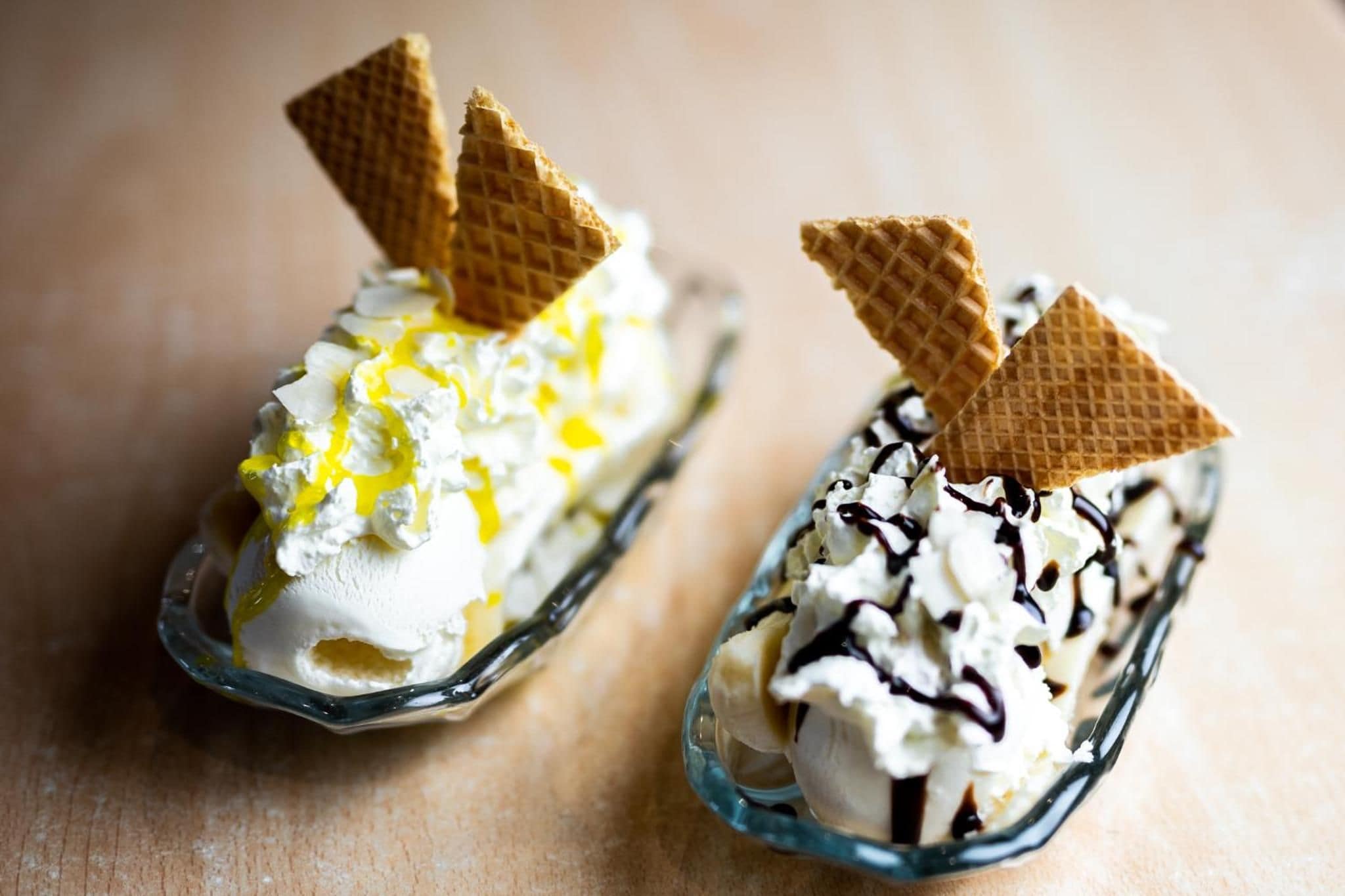 Two dessert cups with whipped cream, yellow syrup, chocolate drizzle, and wafer pieces.