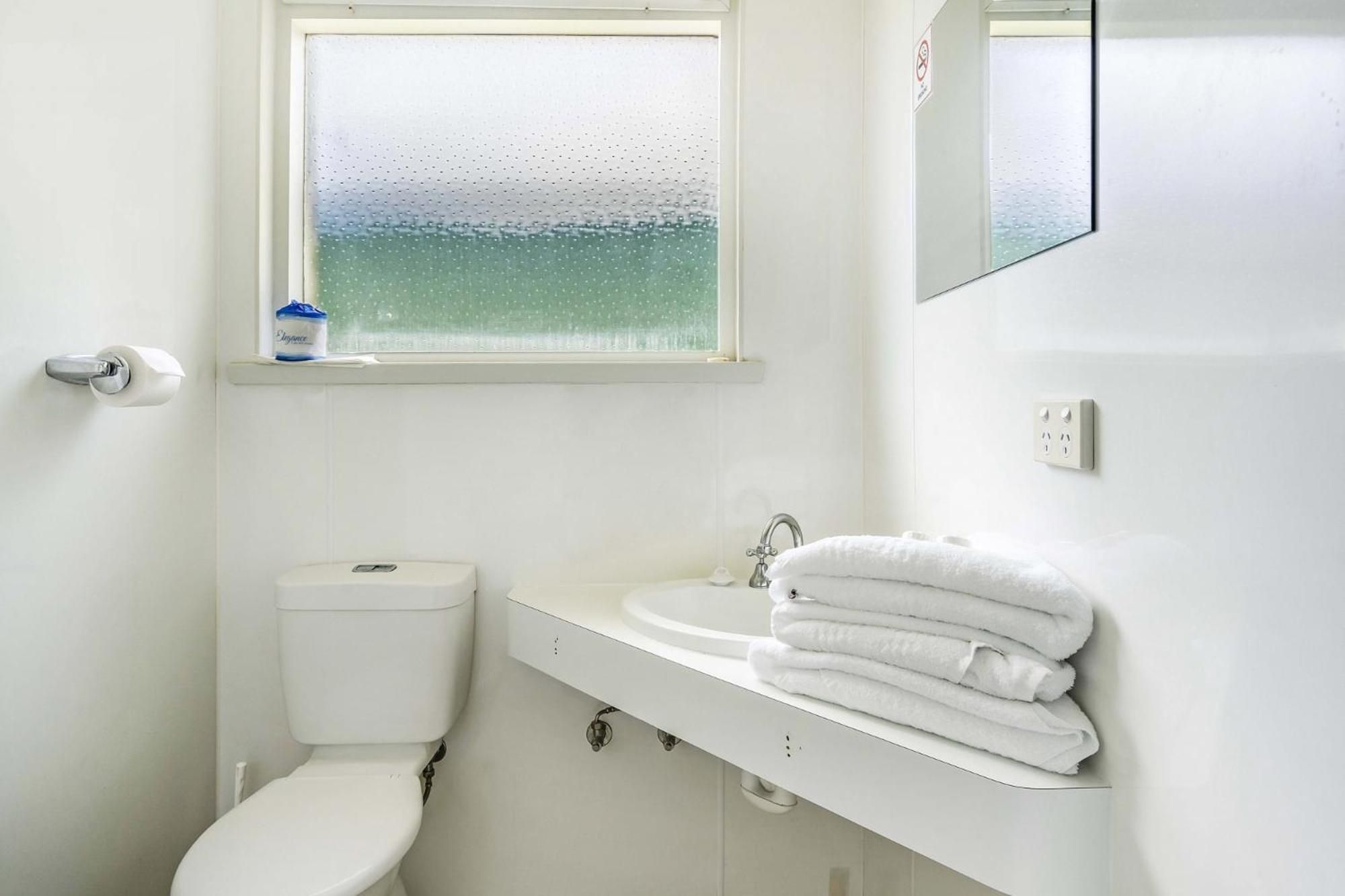 Un baño con inodoro, lavamanos y ventana con vista al mar.