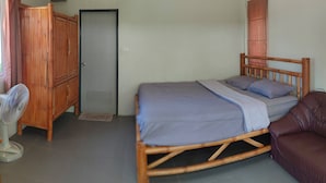 Une chambre avec un lit, une armoire en bois, un ventilateur et un canapé en cuir.