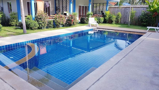 Une piscine aux carreaux bleus, entourée d’un patio couvert aménagé avec du mobilier d’extérieur.