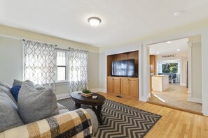 A modern living room with a sofa, a coffee table, and a TV. There is a kitchen area visible in the background.