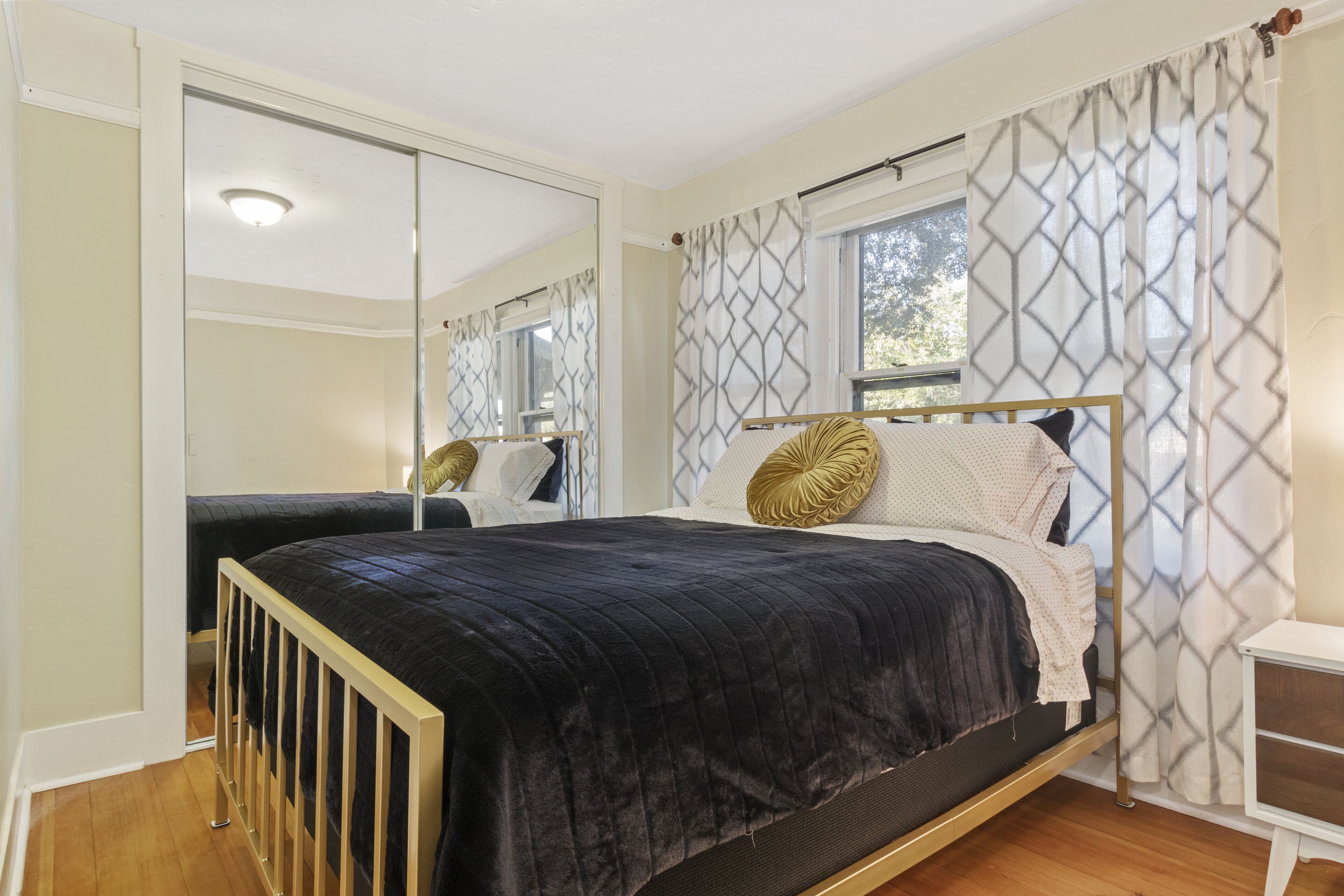 Un dormitorio con cama, mesita de noche, espejo y ventana con cortinas estampadas.