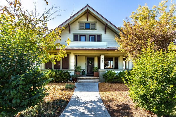 A two-story house with a front porch, a front door, and a small front yard with a pathway leading to the door.