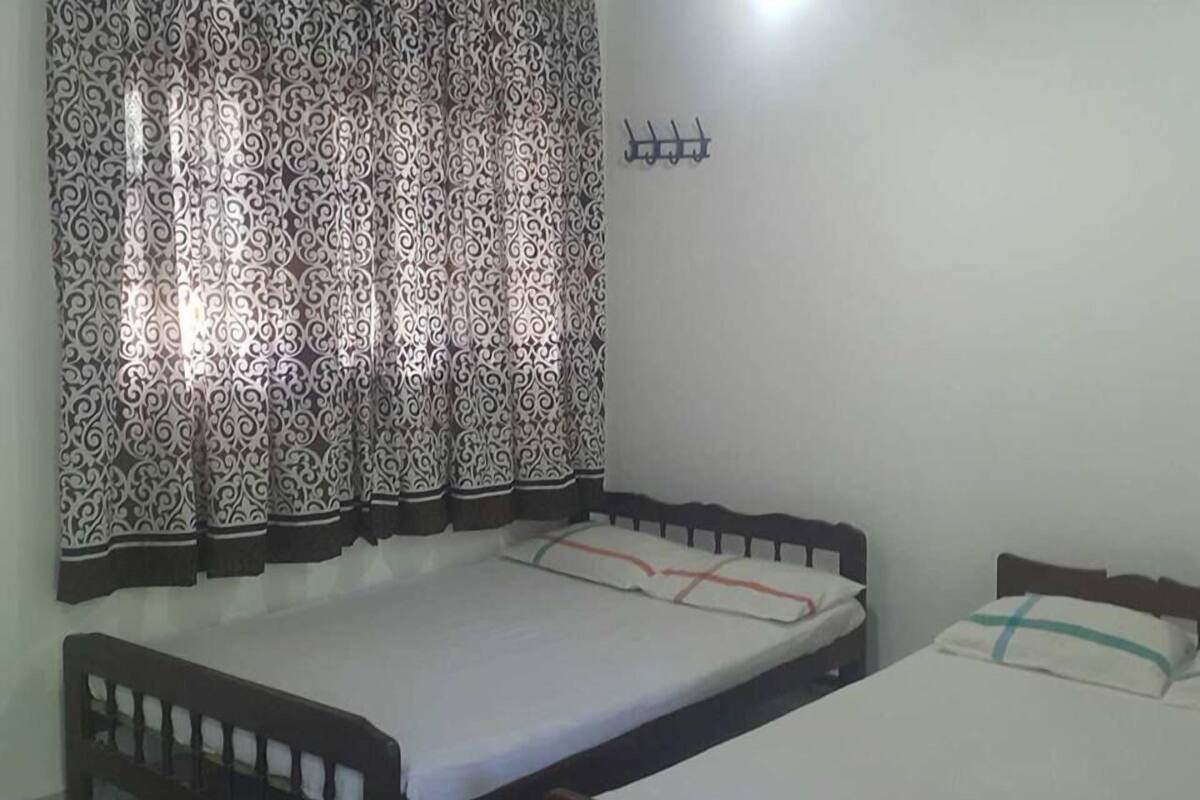 A bedroom with two single beds, a patterned curtain, and a wall-mounted hook.