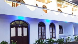 A building with a white facade, multiple arched windows, and a prominent entrance with a wooden door. - Palm Hill Guest House (Talalla)