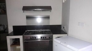 A compact kitchen with a gas stove, oven, and a white refrigerator. - Palm Hill Guest House (Talalla)