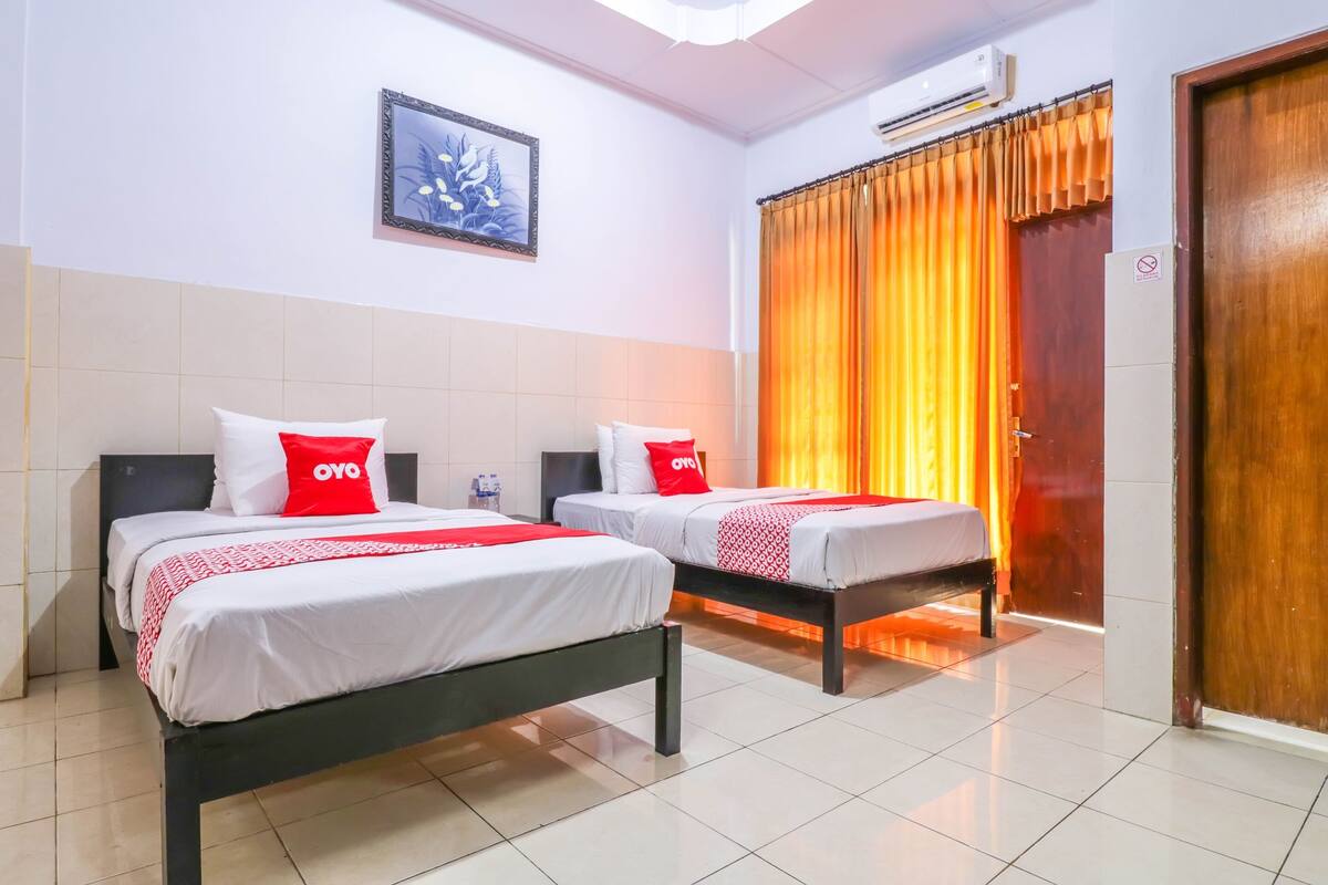 A hotel room with two beds, each with white bedding and red pillows, a framed picture on the wall, and a wooden door.