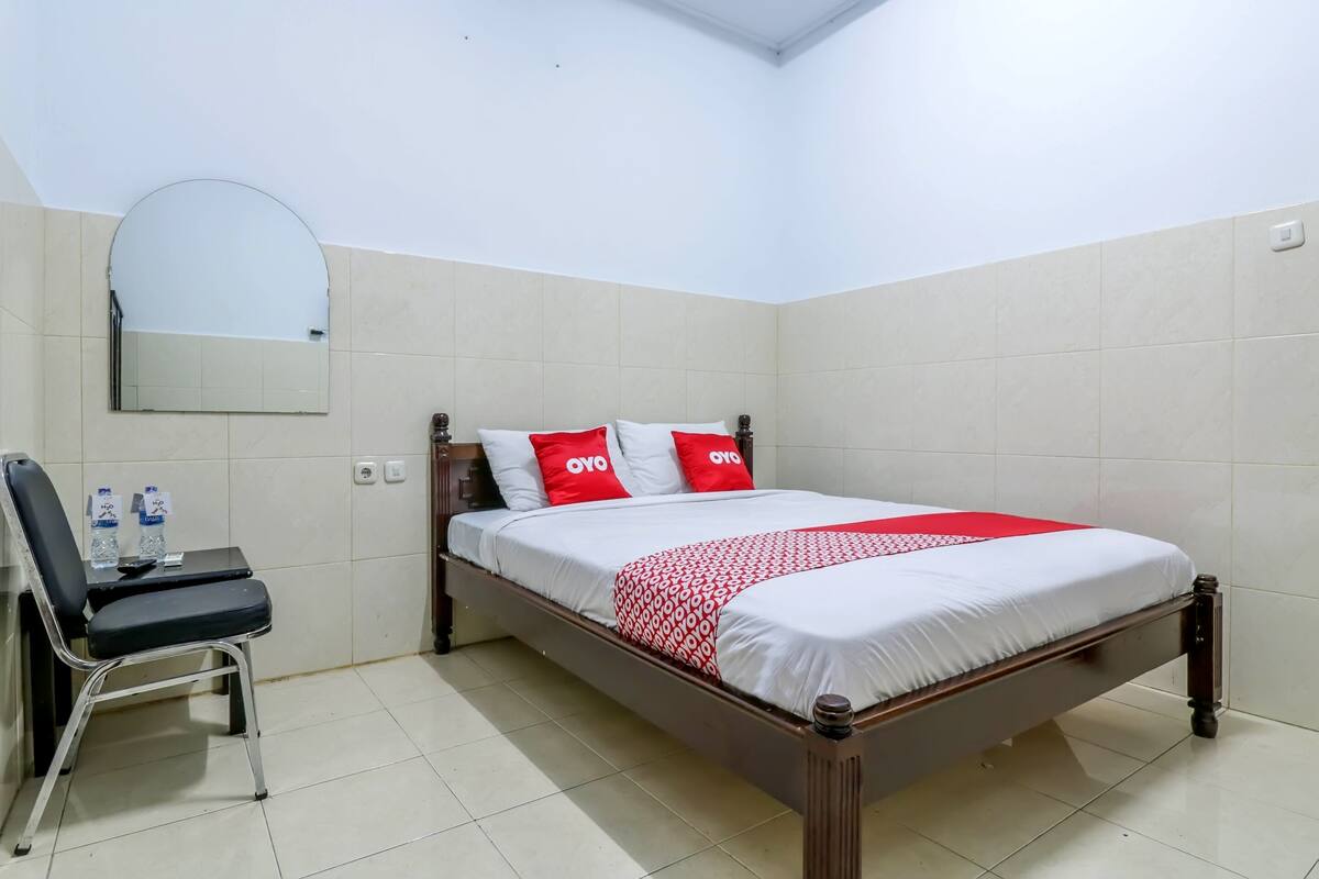 A neatly arranged hotel room with a bed, a chair, a desk, and a mirror.