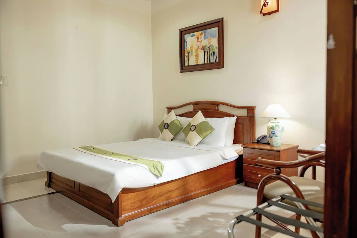 A neatly made bed with a wooden headboard, a bedside table with a lamp, and a framed painting on the wall.