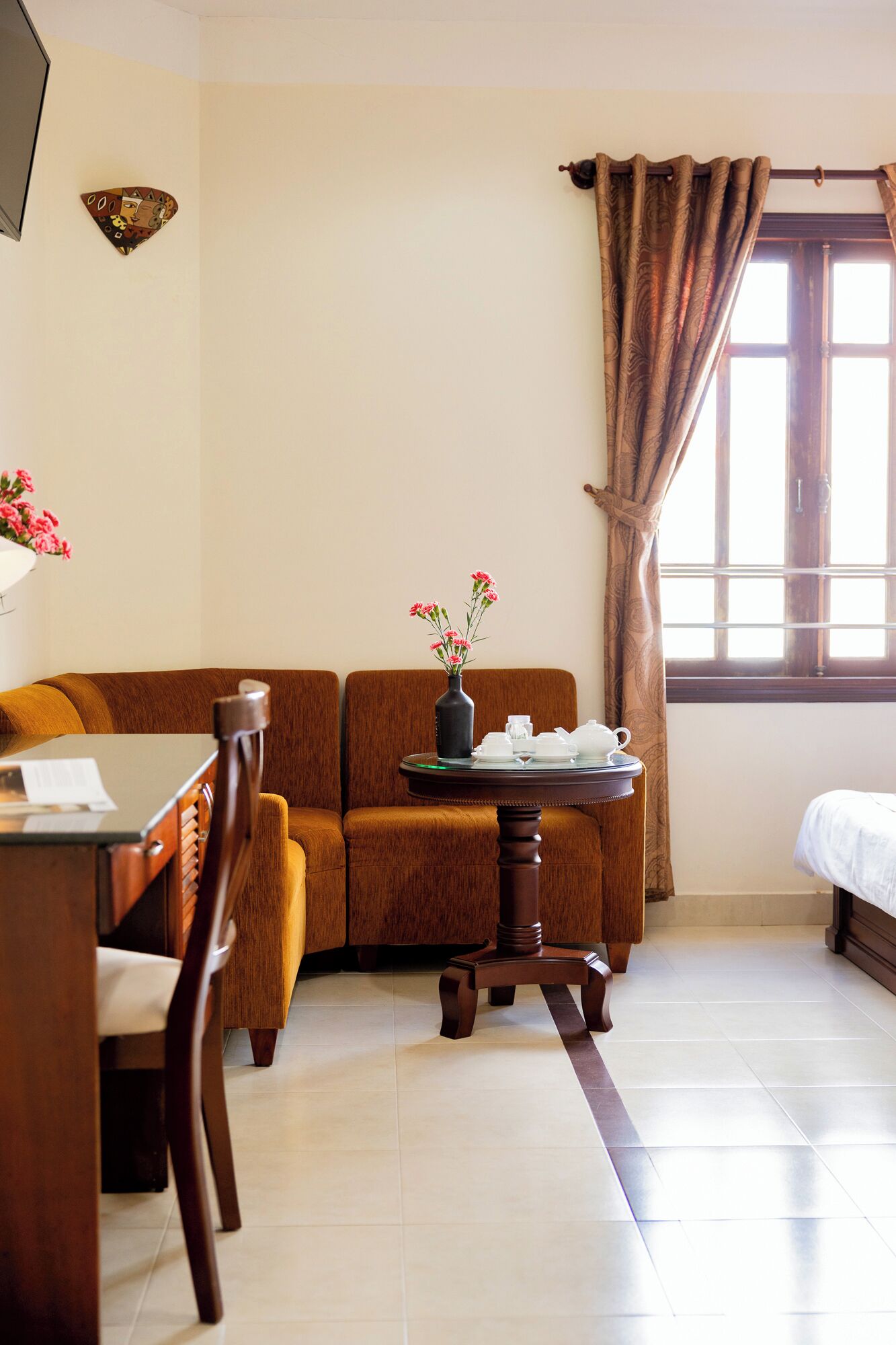 A room with a sofa, a dining table with chairs, a small table with a vase of flowers, and a bed.