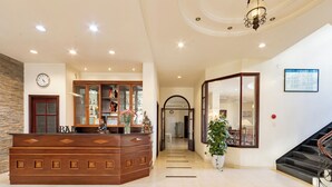 A reception area with a wooden counter, a clock, a glass display cabinet, and a staircase. - Hung Phong Hotel (Xuan Huong - Da Lat)