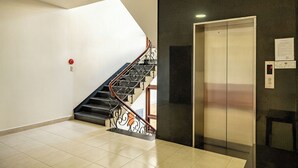 A modern elevator with a digital display, a staircase with ornate metal railings, and a plain wall with a fire alarm. - Hung Phong Hotel (Xuan Huong - Da Lat)