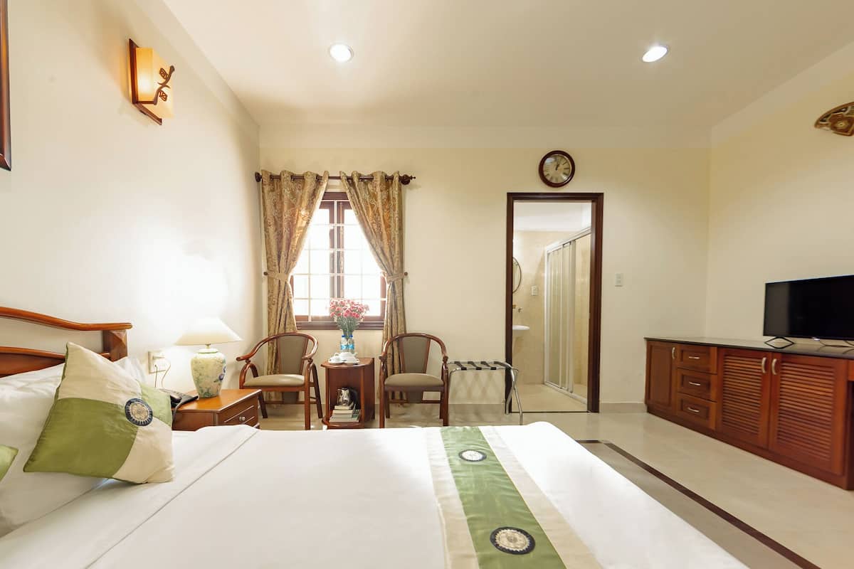 A hotel room with a bed, a desk, a chair, a television, and a bathroom visible through an open door.