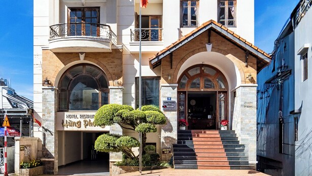 A multi-story hotel with a traditional architectural style, featuring a prominent entrance with steps, balconies, and a flag. - Hung Phong Hotel (Xuan Huong - Da Lat)