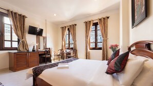 A hotel room with a large bed, a desk with a chair, a television, and windows with curtains. - Hung Phong Hotel (Xuan Huong - Da Lat)
