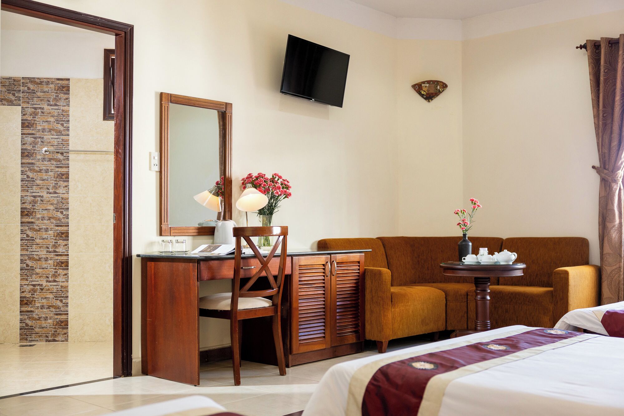 Ein Hotelzimmer mit einem Bett, einem Schreibtisch mit Stuhl, einer Couch, einem Fernseher und einem kleinen Tisch mit Blumen.
