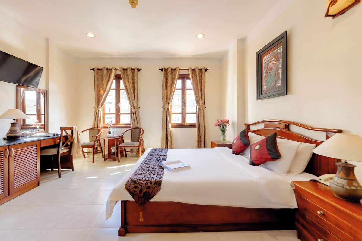 A hotel room with a bed, a desk, a chair, a television, and a window with curtains.