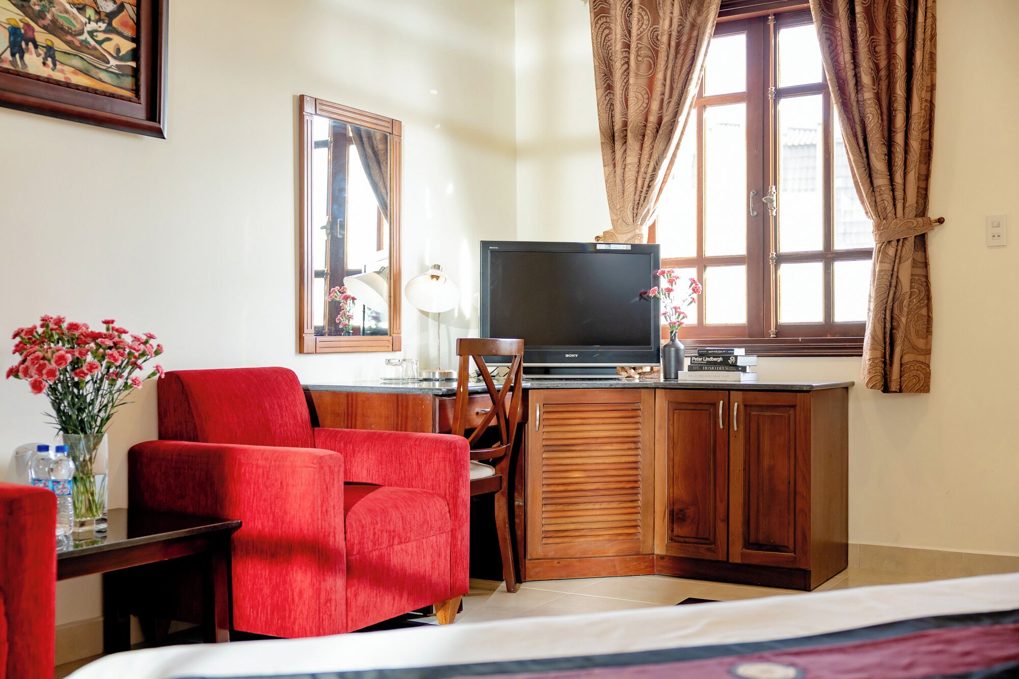 Una habitación de hotel con un sofá rojo, un armario de madera, un televisor y una ventana con cortinas.
