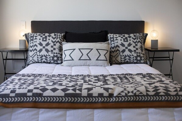 A bed with a patterned bedspread and pillows, flanked by two bedside tables with lamps.