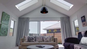 A spacious living room with a high ceiling, skylights, a sofa, a coffee table, and a view of the outside. - The Gallery - Central, Spa Pool, Sleeps 6 (Rotorua)