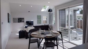 A modern living room with a dining area, large sliding glass doors, and a flat-screen TV. - The Gallery - Central, Spa Pool, Sleeps 6 (Rotorua)