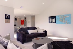 A modern living room with a dark-colored sofa, a round coffee table, and a dining area in the background.