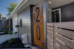 A modern building with a large wooden number '20' sign, a gated entrance, and a small garden with trimmed bushes. - The Gallery - Central, Spa Pool, Sleeps 6 (Rotorua)