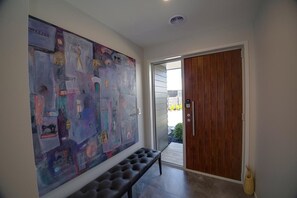 A hallway with a large abstract painting on the wall, a bench, and a wooden door leading to an outdoor area.