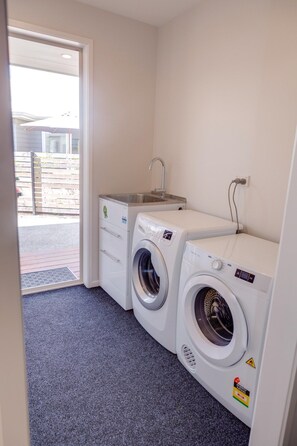 A laundry room with two front-loading washing machines, a sink, and a door leading outside.