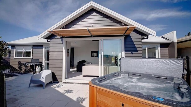 A modern house with a covered patio, a hot tub, and a sliding glass door leading to a bedroom. - The Gallery - Central, Spa Pool, Sleeps 6 (Rotorua)