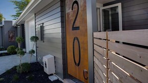 A modern building with a large wooden number '20' sign, a gated entrance, and a small garden with shrubs. - The Gallery - Central, Spa Pool, Sleeps 6 (Rotorua)