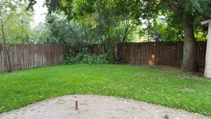A backyard with a wooden fence, a tree, and a paved area. - Cozy home near Sun Valley Resort! (Bellevue)