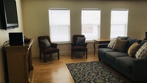 A living room with a wooden floor, a blue sofa, two armchairs, a coffee table, and a flat-screen TV mounted on the wall. - Cozy home near Sun Valley Resort! (Bellevue)