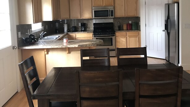A modern kitchen with wooden cabinets, a central island, and a dining area with four chairs. - Cozy home near Sun Valley Resort! (Bellevue)
