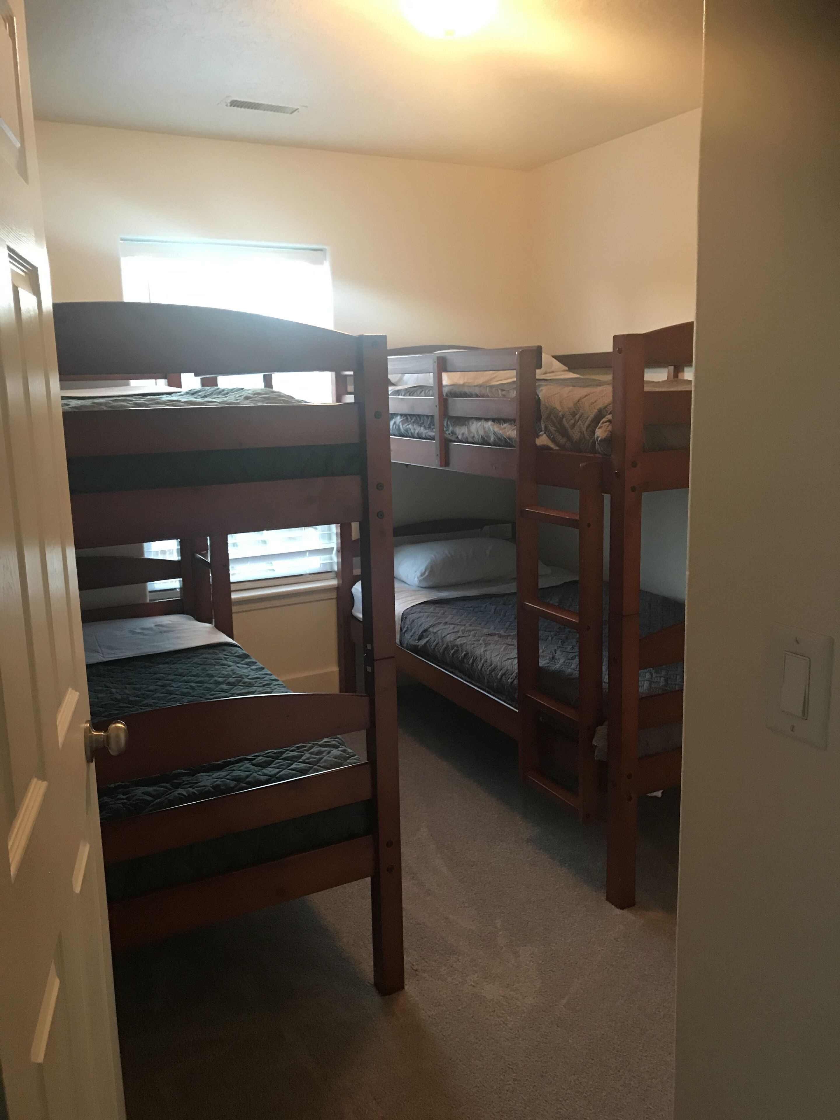 A room with bunk beds, a door, a window, and a light switch.