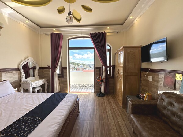 Habitación de hotel con cama, tocador con espejo, televisor montado en la pared, sofá de cuero marrón y vista a la ciudad a través de la ventana.