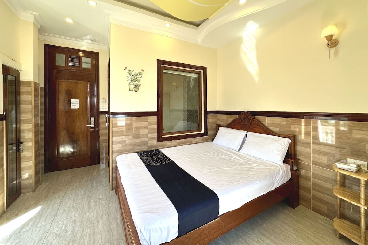 A hotel room with a large bed, a wooden door, a mirror, and a small bedside table.