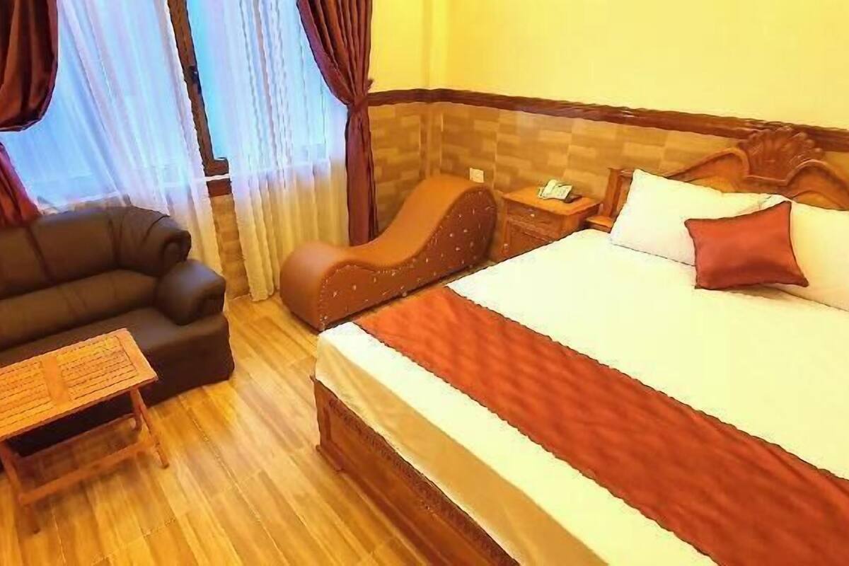 A bedroom with a bed, a sofa, a nightstand, and a wooden table.
