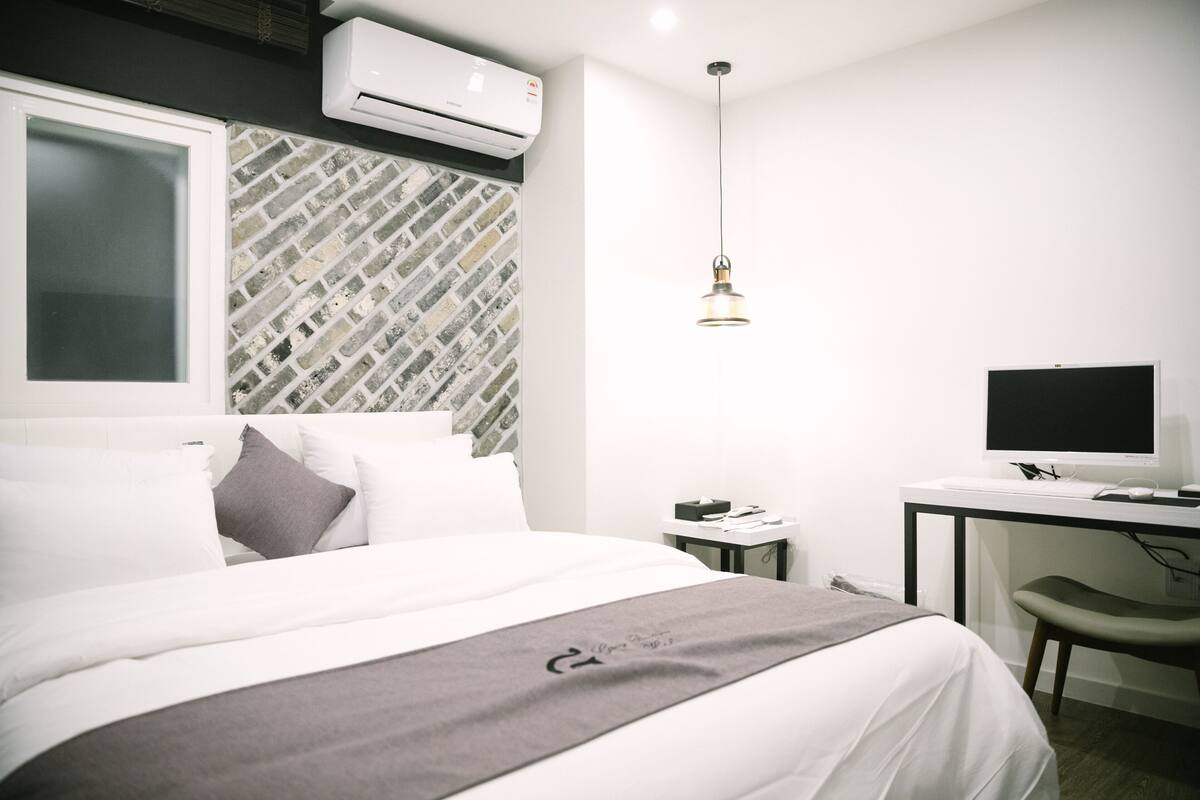 A modern hotel room with a bed, a desk with a computer, and an air conditioning unit.